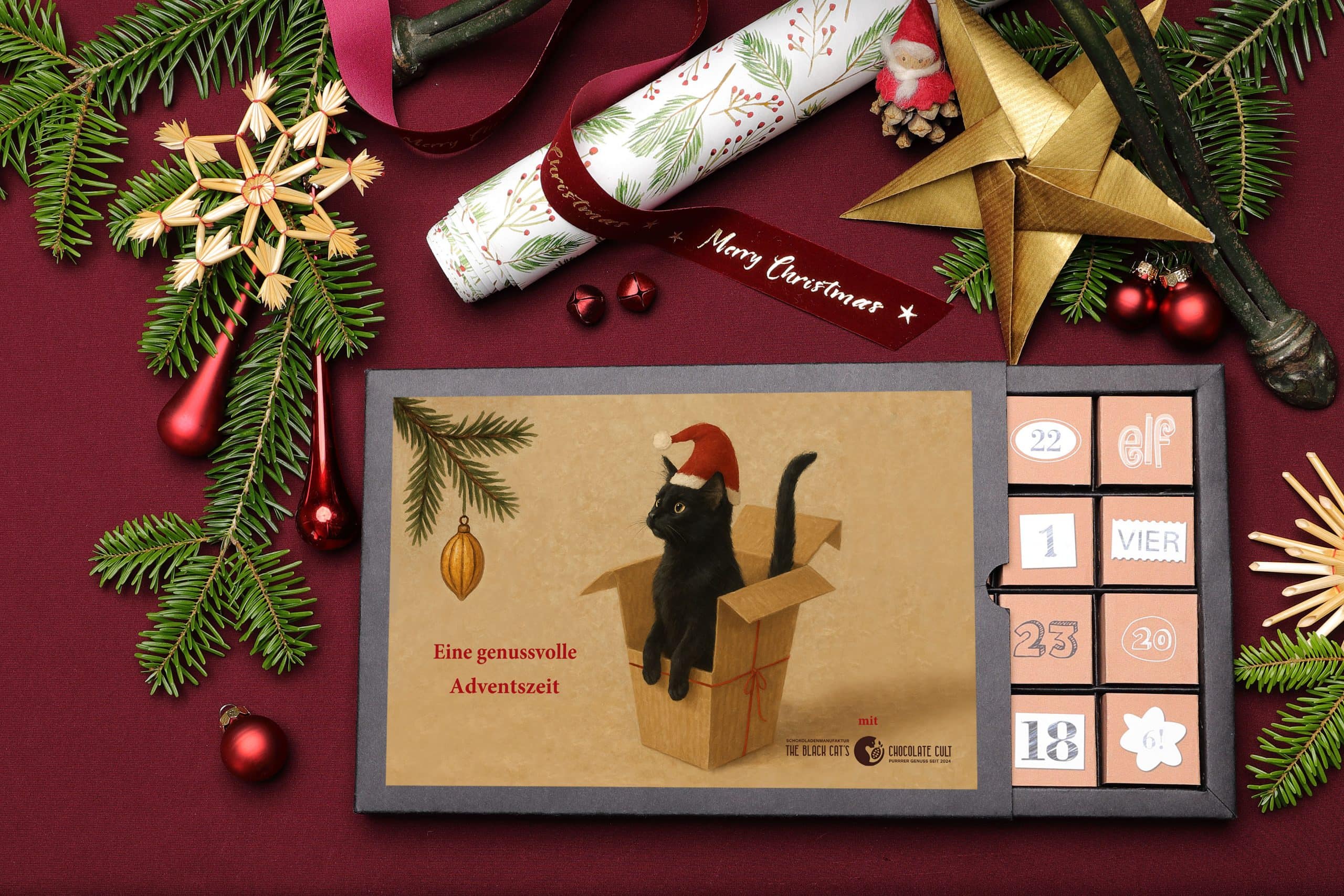 Weihnachtskalender_Slider Weihnachtslicher Geschenketisch mit geöffnetem Adventskalender, schwarzer Kater mit NIkolausmütze auf dem Titel